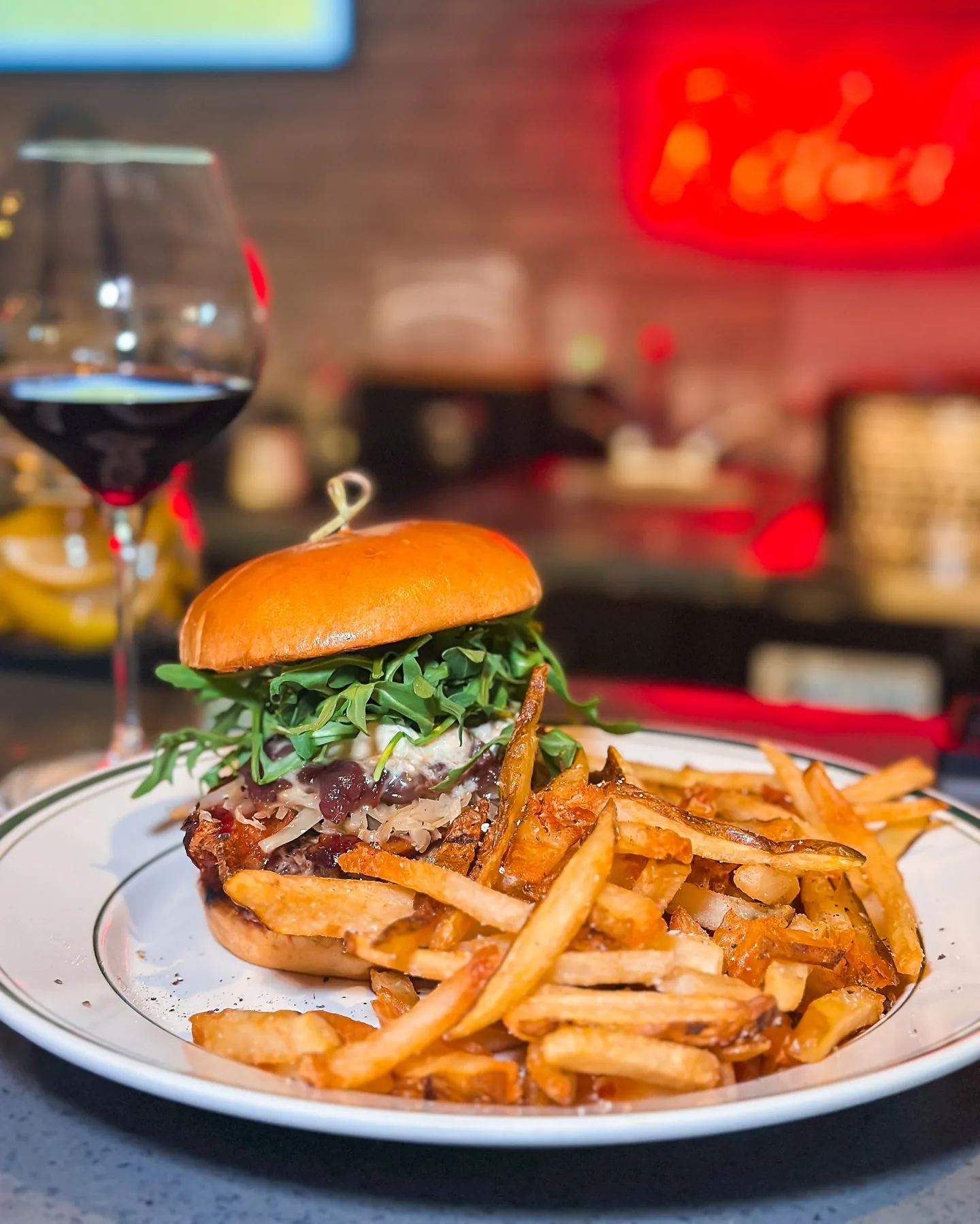 A burger with arugula and hand-cut fries under the neon of the bar