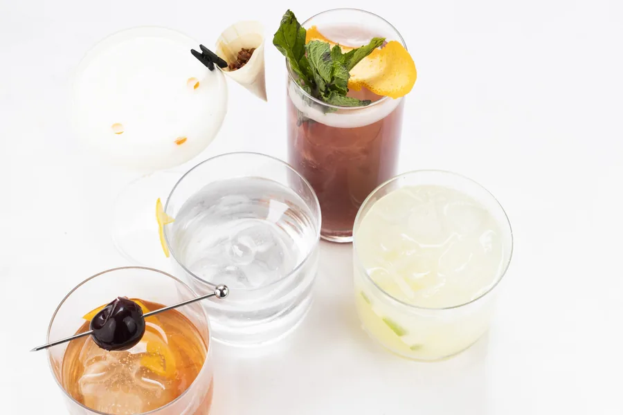 Four cocktails arranged together, garnished and lit from above