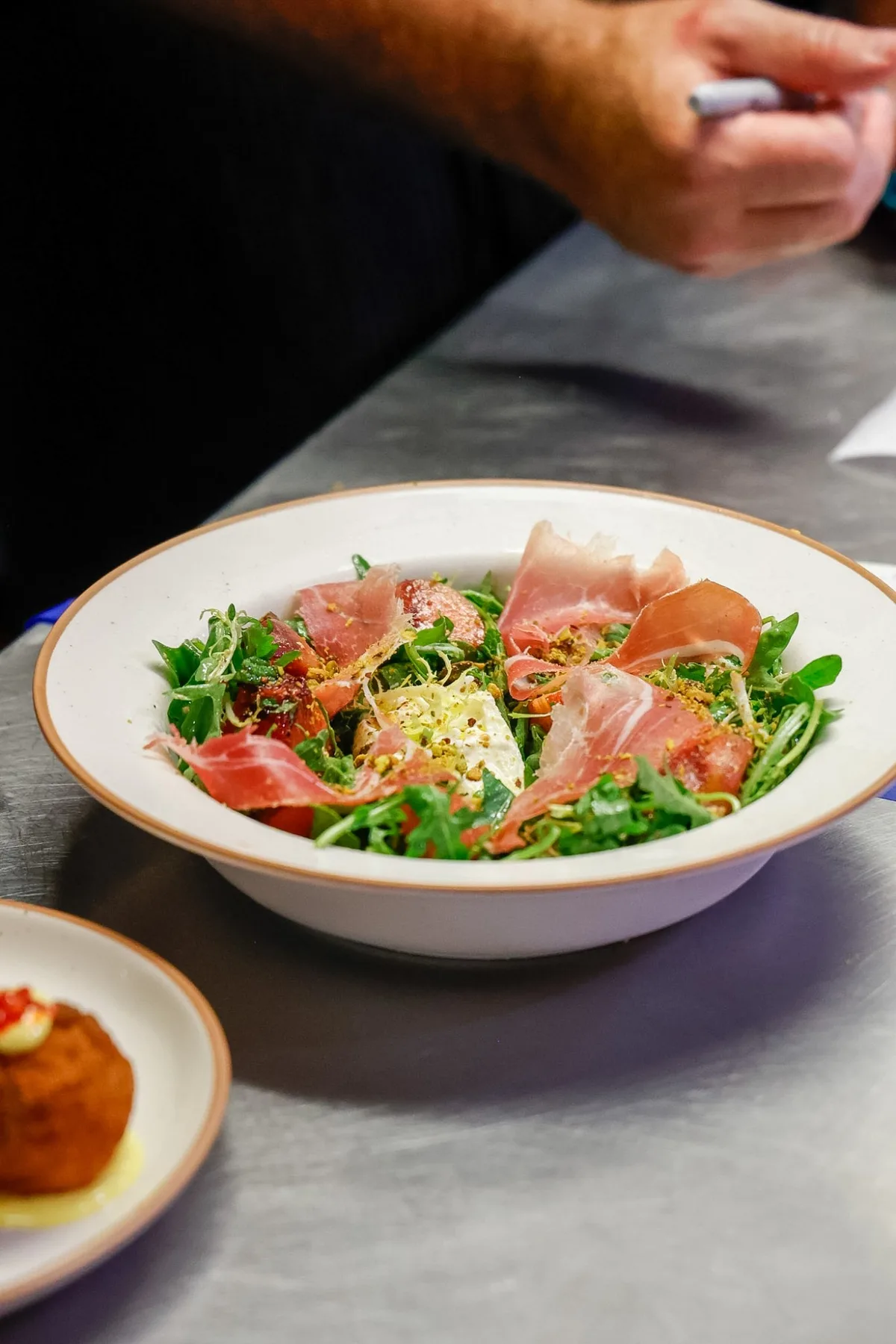 Prosciutto, burrata and peach with rocket and crushed pistachio in a wide bowl