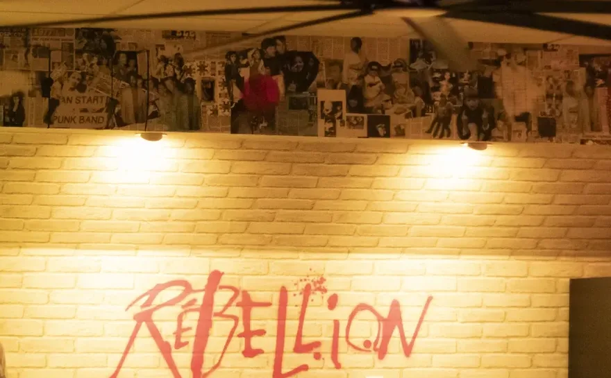 The Rebellion wordmark sprayed across the lit brick wall of the dining room, punk flyers papering the wall above